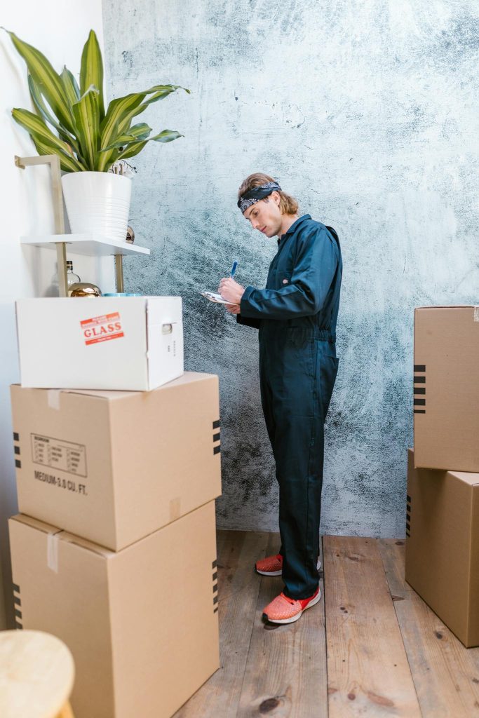 A Caucasian mover in coveralls packing and organizing cardboard boxes indoors.