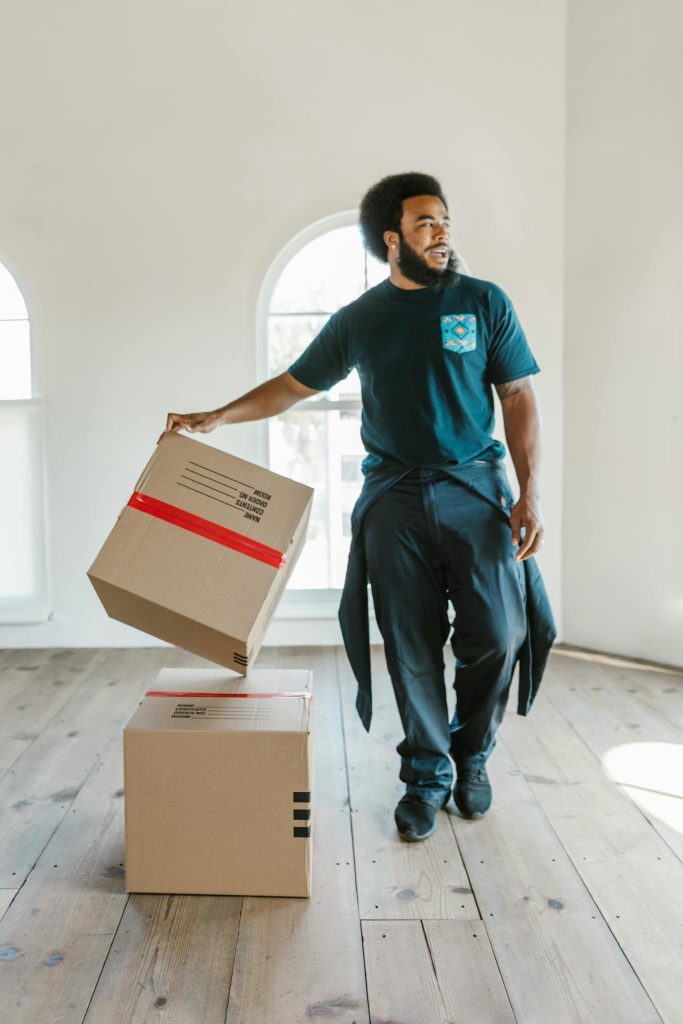A mover carefully handles boxes in a bright, empty room on moving day.