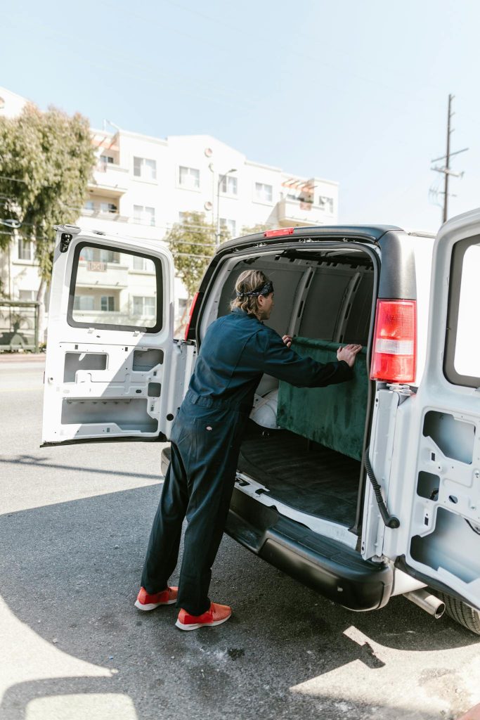 A worker in blue coveralls loads a van on a sunny day for a moving service.
